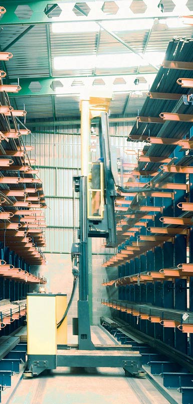 Imagen de una grúa horquilla retráctil de carga lateral en una bodega de perfiles metálicos. 