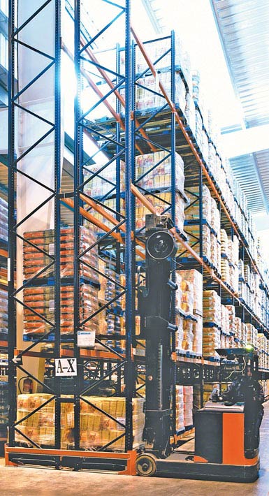 Imagen de una grúa horquilla retráctil de doble fondo utilizada en una bodega de productos alimentarios de gran consumo. 